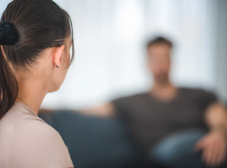 Mujer de espaldas frente a su pareja, sentado al fondo en el sofá Mujer de espaldas frente a su pareja, sentado al fondo en el sofá